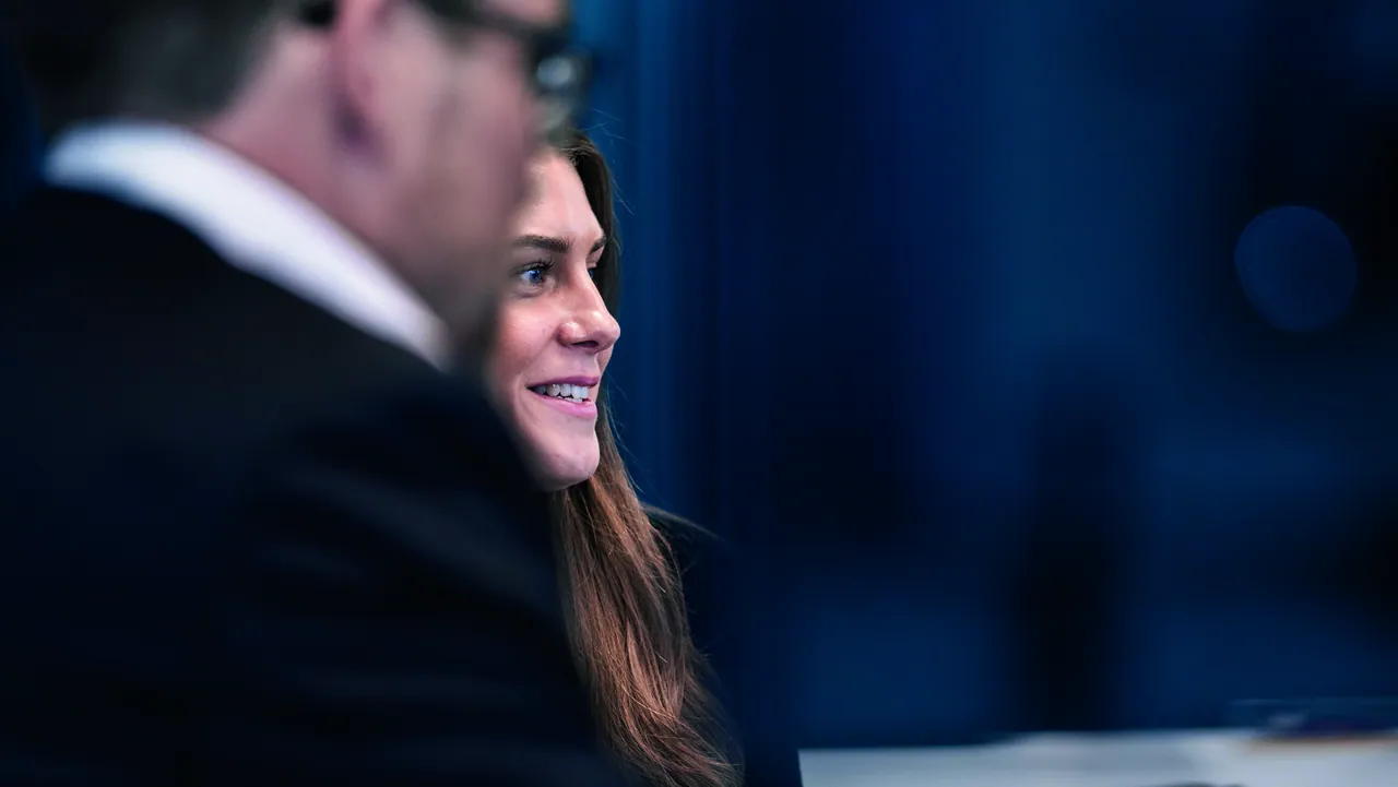 A woman in profile, smiling, beside a colleague in a dark blue office.