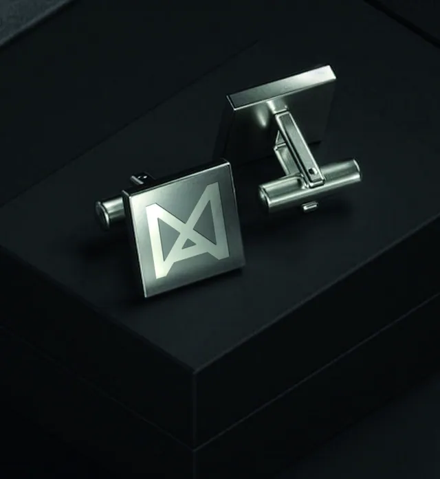 A pair of square silver cufflinks engraved with the Navix logomark, resting on a black box.