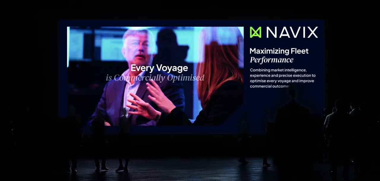 A large event screen in a dark hall showing a video of two people in conversation with the line “Every Voyage is Commercially Optimised”, and beside it the Navix logotype with “Maximizing Fleet Performance”.