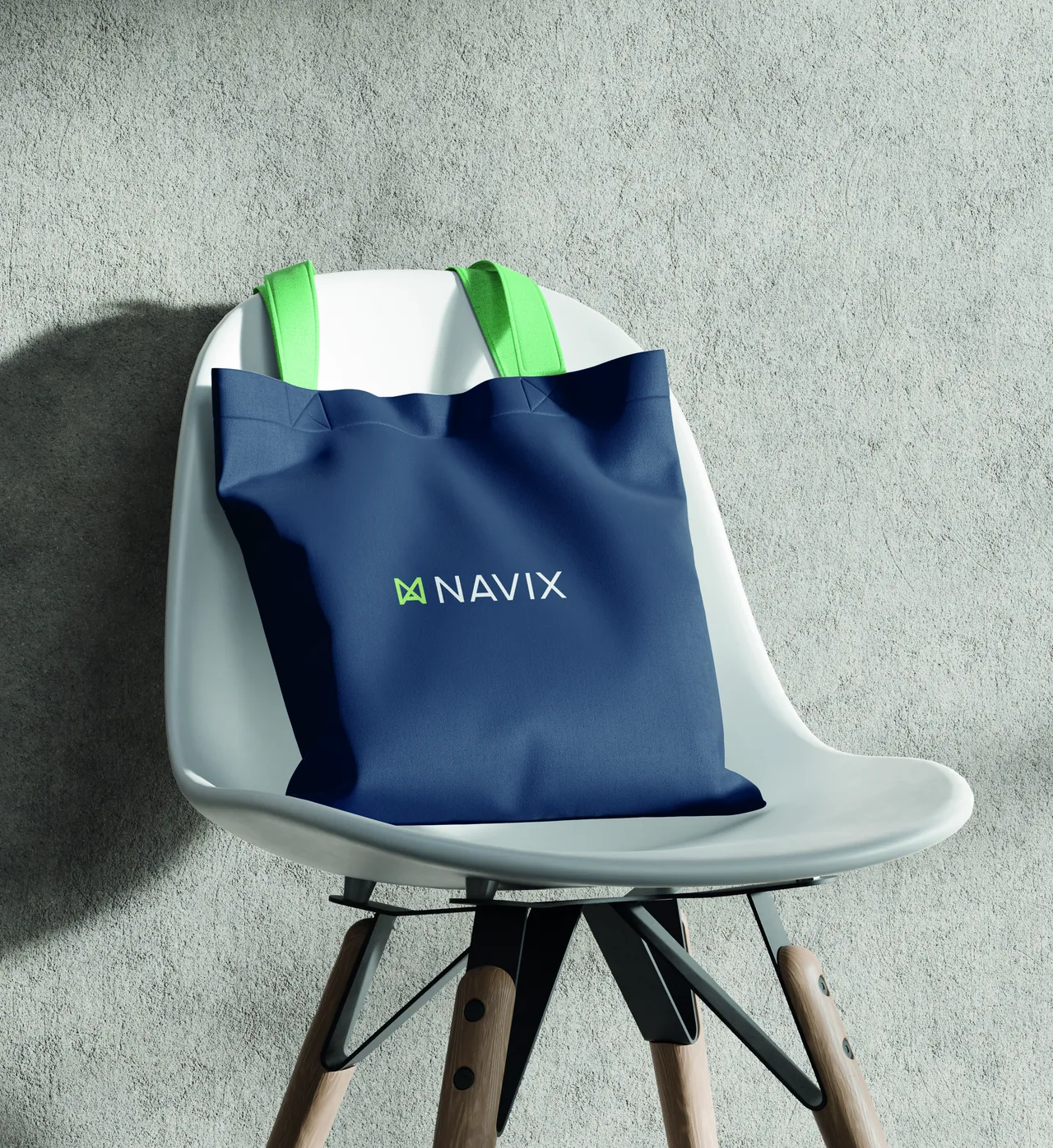 A Deep Sea Blue Navix tote bag with green handles and the negative logotype, hanging on a white chair against a concrete wall.