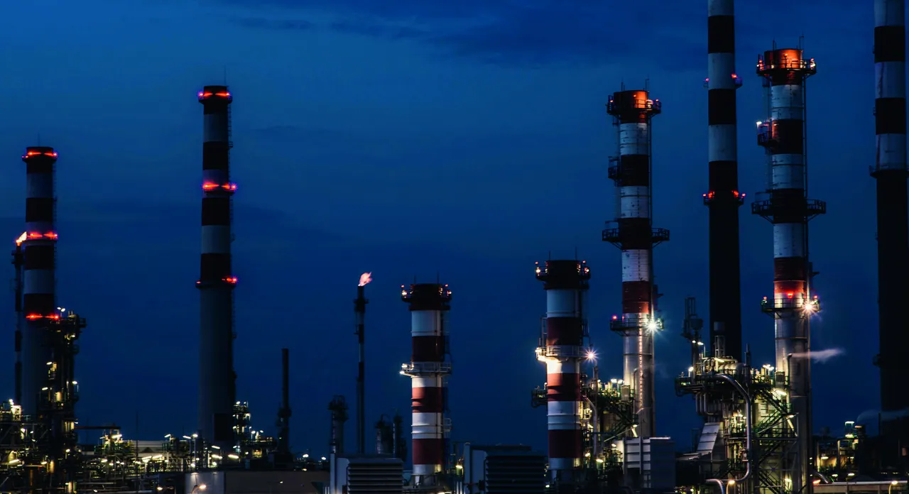 Refinery towers lit up against a deep blue night sky.
