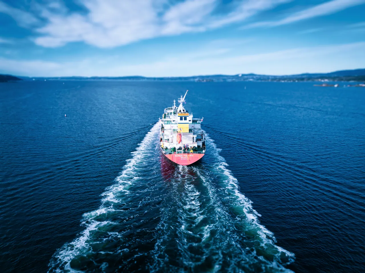 Aerial view of a product tanker underway, leaving a long white wake behind it