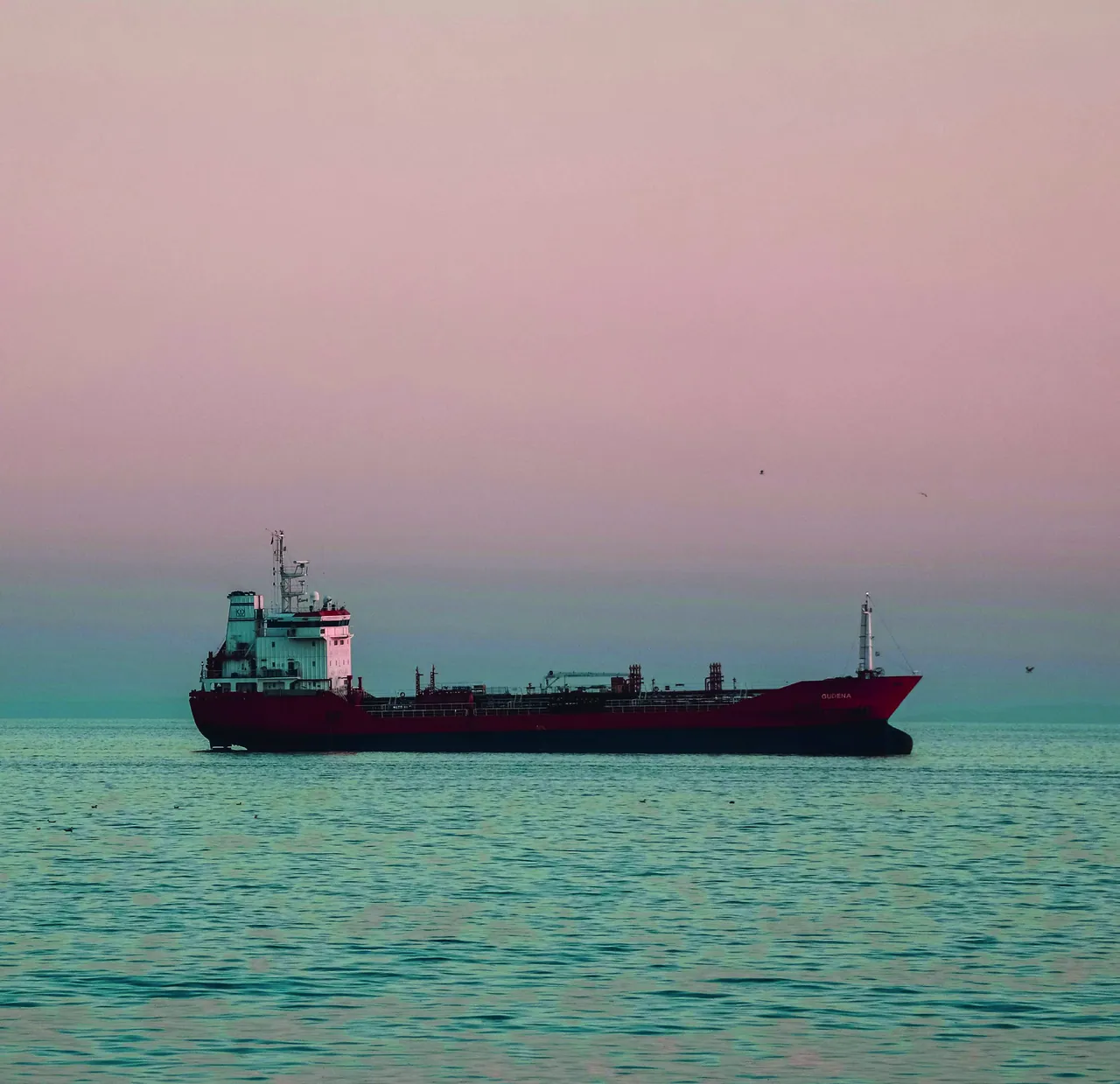Red product tanker at sea under a pink dusk sky